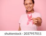Blurred smiling mixed race woman in pink t-shirt hold satin ribbon in her hand. Breast and abdominal cancer awareness, October Pink day on colored background, copy space. Breast cancer support concept