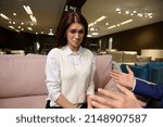 Small photo of Frustrated pretty woman expresses an emotion of desperation, coaxing her husband and insisting on buying new stylish furniture in upholstered furniture mall. Home improvement, interior design concept
