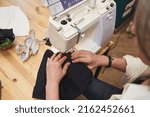 Small photo of Overhead view of a female fashion designer dressmaker tailor seamstress sewing clothes on sewing machine in a tailoring atelier. Creating new garment, fashion designer business start-up concept