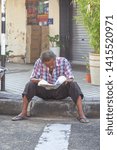 Small photo of Malaysia,May 24, 2019:Man reads a newspaper on footpath at Penan