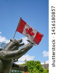 Small photo of Ottawa, Canada - May 24 2009 - A statue named named Territorial Prerogative of a grizzly bear eating a fish with a Canadian flag in the background. It was sculpted by Bruce Garner.
