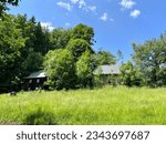 Small photo of two morbid houses at the edge of the forest with a large meadow in front of it in bright sunshine