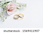 Pink flowers and two golden wedding rings on white background.