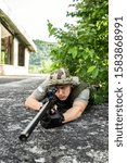 Small photo of Young sniper soldier special force covered with camouflage hat aiming to the enemy waiting for the target to shoot airsoft war game