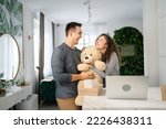 happy couple man and woman boyfriend or husband giving big teddy bear to his girlfriend or wife while having fun at home celebrating pregnancy and family relations valentine concept copy space