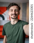 Small photo of One man young adult caucasian male standing at home with brown hair mustaches and beard looking to the camera happy smile confident real people green t shirt UGC selfie user generated content