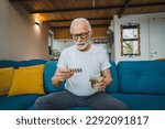 Small photo of One senior man caucasian male grandfather sit at home hold blister pack of drug tablet painkillers or vitamin supplement read label ready to take medicine real person copy space