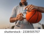 close up on hands midsection of unknown caucasian man teenager open plastic bottle of water outdoor in sunny day doing sports with basketball