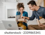 Small photo of young couple man and woman boyfriend and girlfriend or husband and wife exchange gifts at home giving presents to each other and opening box happy smile celebrate valentine holiday or birthday