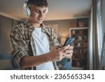 Small photo of Portrait of teenage boy stand at home use headphones ans smartphone to play music or watch video podcast at home