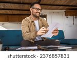 Small photo of One man mature caucasian male work at home hold paper document sign insurance contract or read report enjoy good news in letter receive official paper about tax refund credit loan approval