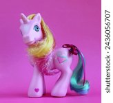 Small photo of Randburg, South Africa: 02-23-2024: Pretty pink unicorn toy isolated on a bright pink background. My Little Pony G3 Rarity. Side view. Side lit. Shallow depth of field.