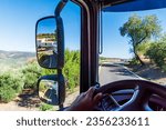 Small photo of View from the cab of a truck of a narrow road and the rearview mirror where you can see the sharp turn of the tank trailer.