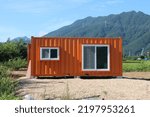 Small photo of Orange shipping container temporary office on construction site near mountain town