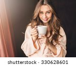 Soft photo of fresh young woman in pink tender bathrobe drink tea and smiling. Pretty girl with perfect  wavy hairs enjoying  early  sunny morning.