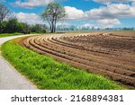 Beautiful rural dutch farm landscape, freshly tilled plowed cropland field, symmetrical right curved parallel arable furrows, empty cycle path - Netherlands near Roermond 