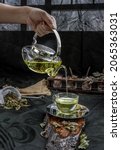 Small photo of A Hot pandan leaf tea with indian marsh fleabane plant leaves and Safflower dried (Saffron substitute) is poured from the glass teapot into a glass with tea herbal and tea leave. Selective focus.