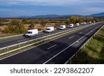 Small photo of Eight white minivans are moving in a convoy on the highway. White delivery van on the highway. White modern delivery small shipment cargo courier van moving fast on motorway road to city urban suburb.