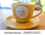 Wake up, message of the brand new day. Sign letters. Close up detail of coffee cup. Blurry background.