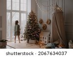 A 10-year-old girl stands at the window in the children's room and waits for santa claus. Christmas Eve. New Year's Morning. The mood is waiting for the holiday. Christmas atmosphere. Stylish interior