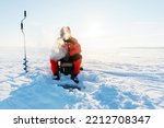 Small photo of Winter fishing. An angler in a red jumpsuit catches fish in very cold weather. Severe frost and profuse evaporation during breathing. Unrecognizable person. copy space