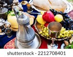 Small photo of A metal jug and a glass for wine on the background of a table with fresh fruits. Food and utensils in the medieval style. Reconstruction of the life of the ancient peoples of the times of chivalry.