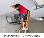 Man inspecting garage attic. Male homeowner climbing wooden pull down attic ladder.