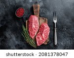 Fresh Raw Top Blade or flat iron beef meat steaks on a butcher cutting board. Black background. Top View