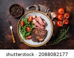 Small photo of BBQ Grilled rib eye steak, fried rib-eye beef meat on a plate with green salad. Dark background. top view