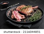 Small photo of Barbecue sliced rib eye Tomahawk beef (veal) steak on a plate with pink salt. Black background. Top view