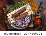 Small photo of Turkish Adana Kebab from mince lamb beef meat on Skewer with flatbread and onion. Dark background. Top view.