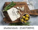 Danish blue cheese on a wooden board with olives and rosemary. Gray background. Top view.