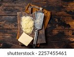 Piece of semi hard cheese and grated cheese with grater. Wooden background. Top view.