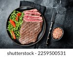 Grilled medium rare flank beef steak with salad in a plate. Black background. Top view.