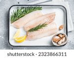 Small photo of Uncooked Raw cod loin fillet steaks with herbs in kitchen tray. Gray background. Top view.