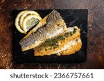 Roast sea bass fillet with lemon and thyme, seabass fish. Dark background. Top view.