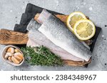 Small photo of Fresh Raw Sea Bass fillets, Branzino fish with thyme and lemon. Gray background. Top view.