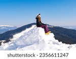 Women alpine girl in winter overalls sitting on snow hill looking at high Carpathian mountains at winter ski resort holiday, outdoor nature landscape, Ukraine, Europe.aerial view.