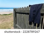 Small photo of A shorty wetsuit is hanging on a fence to dry, its been having fun in the sea nearby.
