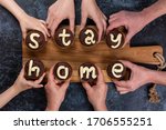 Concept flat lay Stay Home. Many hands of different ages of people reach out and hold chocolate muffins, with cream letters. Eight cupcakes make up the two words. Big family on self-isolation.