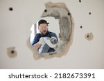 Demolition of an old house. Demolition of unnecessary walls with hand-held impact hammer. A view of an experienced construction worker trying with all might to enlarge hole in wall.