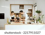Small photo of Happy young mother and father with adorable daughter standing at modern kitchen dressing domestic fresh kneaded pizza together using cheese mushrooms.