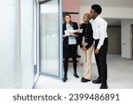 Small photo of With a gracious smile, the blonde real estate agent directs the attention of the African couple to the magnificent scenery visible from the balcony, taking their breath away.