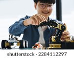 Small photo of Asian teenager students doing or playing robot arm and robotic cars homework project in house disassemble the circuit and coding. technology of robotics programing and STEM education concept.