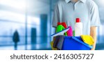 Small photo of Charwoman standing with a bucket and cleaning products on blurred office modern building background.