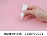 Female hand squeezes cream or gel from tube on pink background. Сosmetic bottles for beauty or medicine products