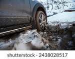 Small photo of The side view of a car reveals the vehicle's wheel deeply embedded in snowy terrain, hinting at the perils of traversing icy roads. The surrounding environment speaks to the solitude and risks of wint