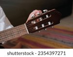 Crop anonymous musician in white clothes tuning pegs of acoustic guitar skillfully for playing songs
