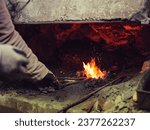 Small photo of Crop unrecognizable male forger in protective gloves standing tongs and burning metal in furnace while working in blacksmith workshop