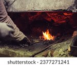Small photo of Crop unrecognizable male forger in protective gloves standing tongs and burning metal in furnace while working in blacksmith workshop